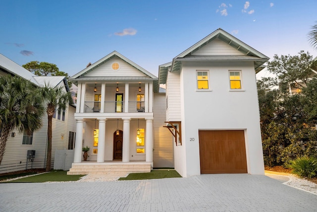 greek revival inspired property featuring a balcony, a garage, decorative driveway, and stucco siding