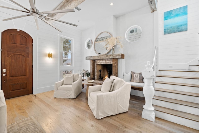 living area with a warm lit fireplace, ceiling fan, stairway, and light wood-style flooring