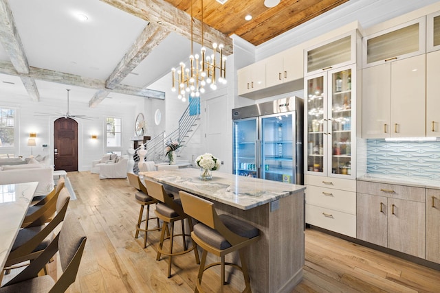 kitchen featuring glass insert cabinets, a breakfast bar area, open floor plan, built in refrigerator, and pendant lighting