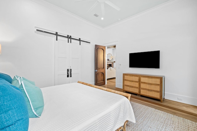 bedroom featuring crown molding, visible vents, a barn door, wood finished floors, and baseboards