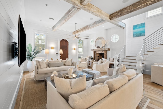 living room featuring light wood finished floors, beamed ceiling, a fireplace, and stairway