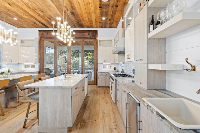 kitchen with an island with sink, glass insert cabinets, and a notable chandelier