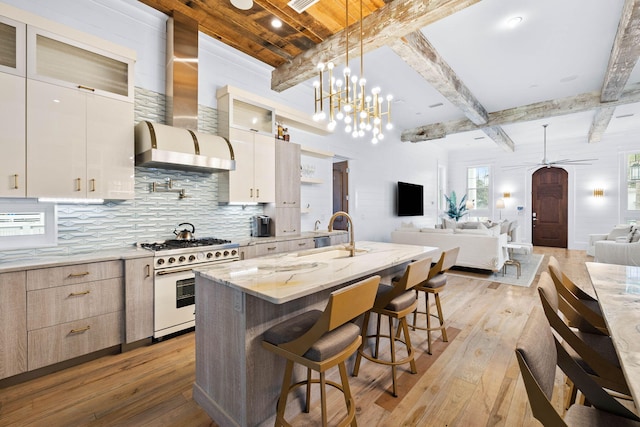 kitchen featuring wall chimney exhaust hood, glass insert cabinets, open floor plan, a kitchen island with sink, and high end stove