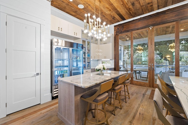 kitchen featuring light stone counters, high end fridge, hanging light fixtures, wood ceiling, and white cabinetry