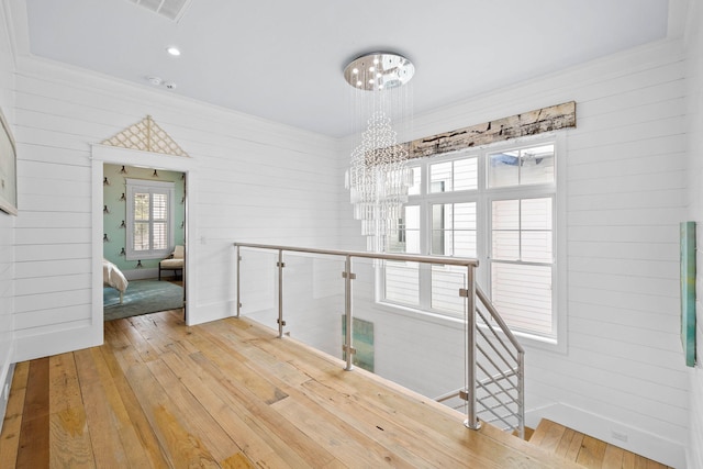 corridor with a chandelier, light wood-style flooring, visible vents, and an upstairs landing