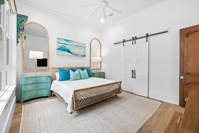 bedroom featuring a barn door, wood finished floors, a ceiling fan, visible vents, and crown molding