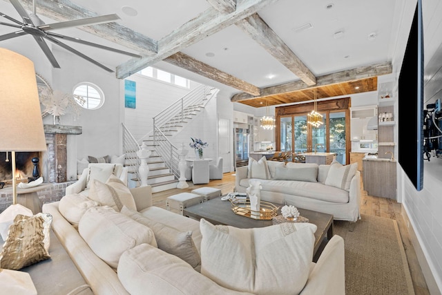 living room with light wood-type flooring, stairway, beam ceiling, and ceiling fan with notable chandelier