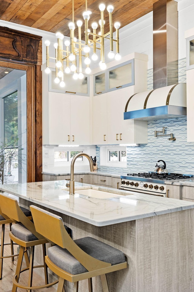 kitchen with light stone counters, tasteful backsplash, glass insert cabinets, white cabinetry, and wall chimney range hood