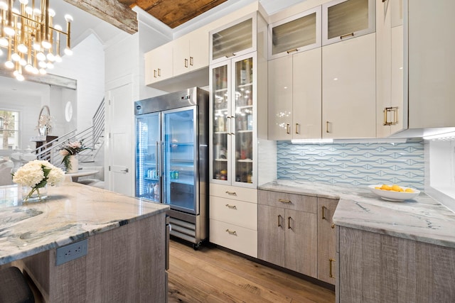 kitchen featuring built in refrigerator, light stone countertops, glass insert cabinets, and decorative light fixtures