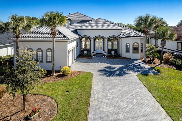 mediterranean / spanish house with a tile roof, french doors, decorative driveway, stucco siding, and a front lawn