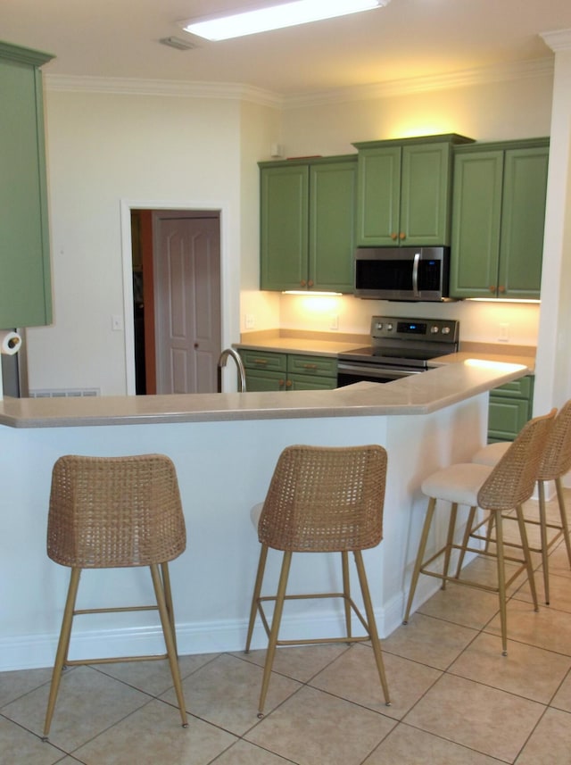 kitchen with stainless steel appliances, green cabinetry, ornamental molding, and a kitchen bar