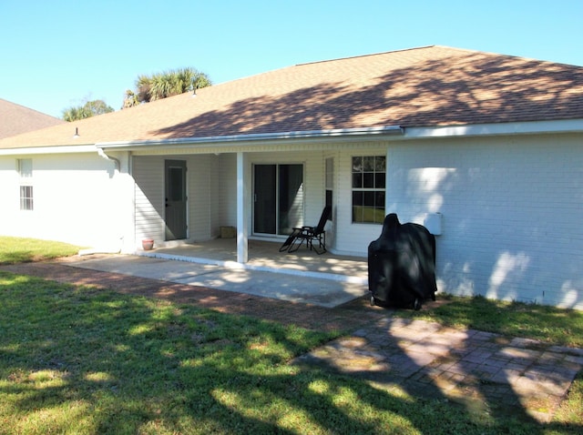 back of property featuring brick siding, roof with shingles, a lawn, and a patio