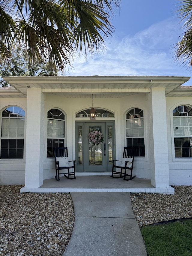 property entrance featuring a porch and brick siding