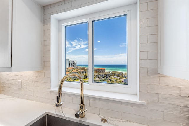 interior details featuring a water view, light stone countertops, white cabinetry, and a sink