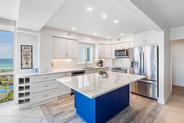 kitchen with light stone counters, stainless steel appliances, visible vents, white cabinets, and a sink