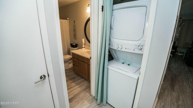 laundry room with a sink, stacked washing maching and dryer, laundry area, and wood finished floors