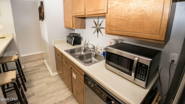 kitchen with a sink, light countertops, brown cabinetry, light wood finished floors, and stainless steel microwave