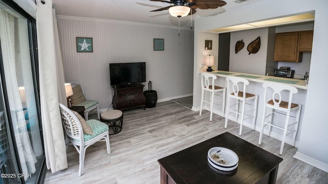 living area with ornamental molding, light wood-style floors, baseboards, and a ceiling fan