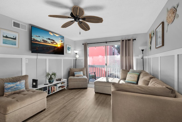 living room featuring a ceiling fan, visible vents, a decorative wall, and wood finished floors