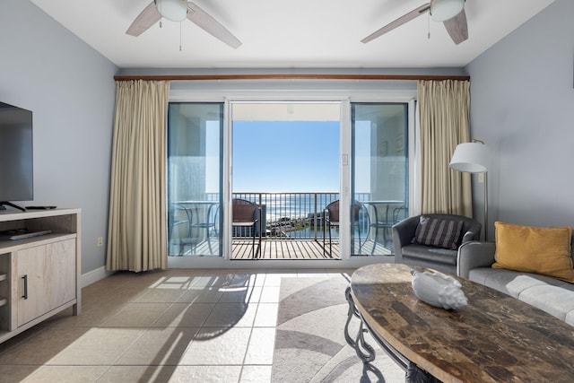 living room with light tile patterned floors, a water view, a ceiling fan, and baseboards