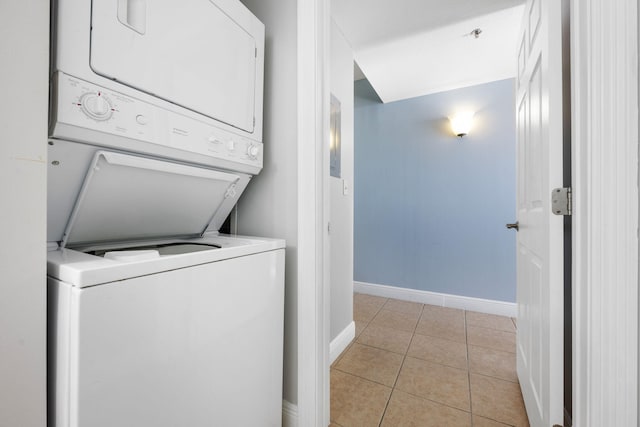 washroom with laundry area, light tile patterned flooring, stacked washer and clothes dryer, and baseboards