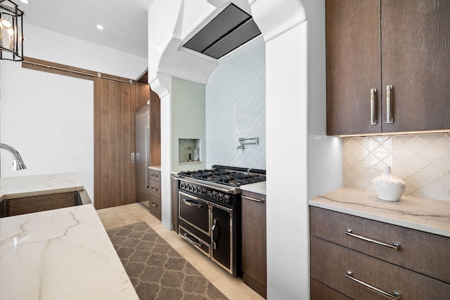 kitchen featuring decorative backsplash, a sink, dark brown cabinets, light stone countertops, and double oven range