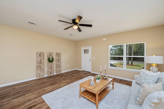 living room featuring a ceiling fan, visible vents, baseboards, and wood finished floors