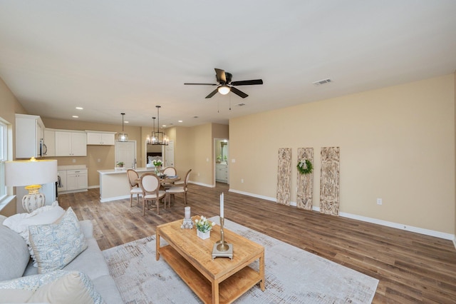 living room with ceiling fan with notable chandelier, light wood-style flooring, visible vents, and baseboards