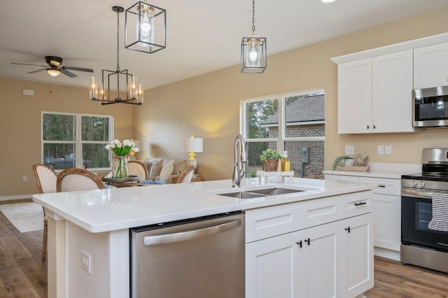 kitchen featuring white cabinets, an island with sink, stainless steel appliances, light countertops, and a sink