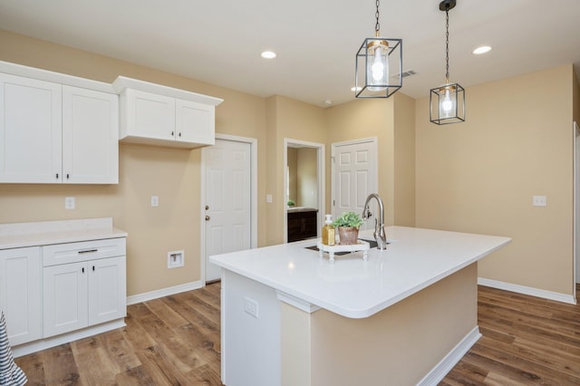 kitchen with light countertops, white cabinets, and an island with sink