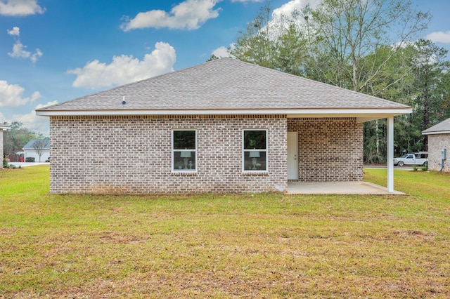 rear view of property with a patio area, a shingled roof, a lawn, and brick siding