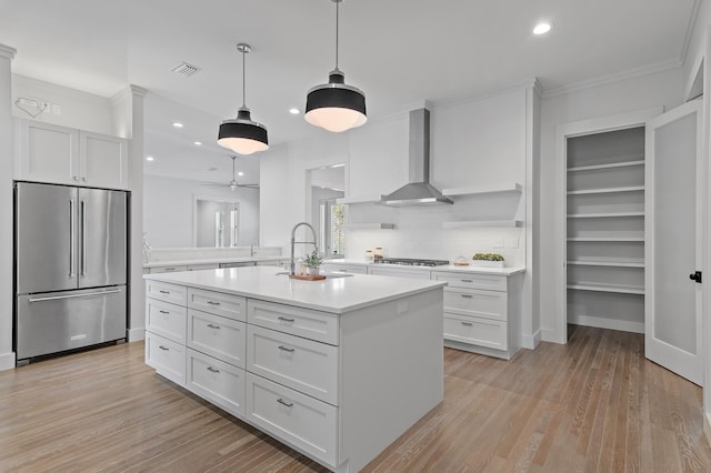 kitchen featuring light countertops, white cabinets, a sink, high quality fridge, and wall chimney exhaust hood