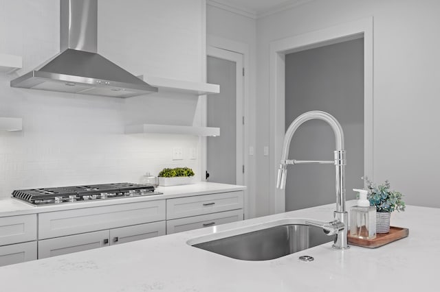 kitchen featuring tasteful backsplash, stainless steel gas stovetop, white cabinetry, a sink, and wall chimney exhaust hood