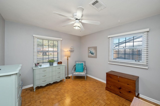 living area featuring baseboards, visible vents, and a ceiling fan