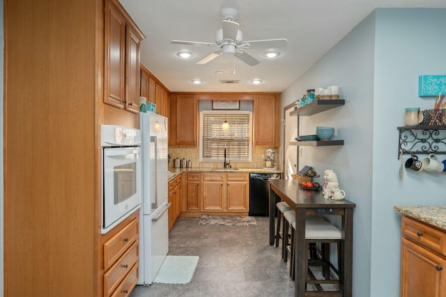 kitchen with light stone counters, tasteful backsplash, visible vents, a sink, and white appliances