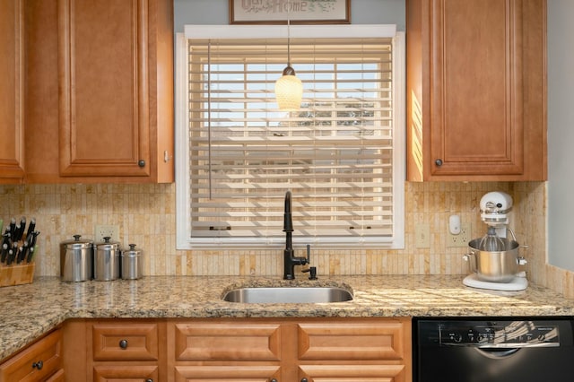 kitchen featuring black dishwasher, light stone counters, brown cabinetry, and a sink