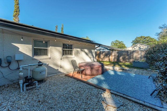 rear view of property featuring a patio area, brick siding, fence, and a hot tub