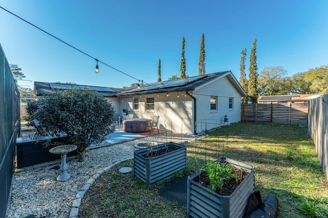 rear view of property with a lawn, solar panels, a jacuzzi, a fenced backyard, and brick siding