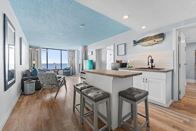 kitchen featuring a breakfast bar, open floor plan, white cabinetry, a sink, and wood counters