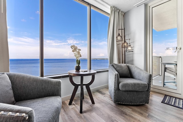 living area with a textured ceiling, a water view, wood finished floors, and baseboards