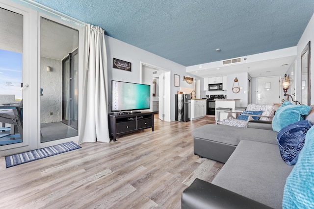 living room with a textured ceiling, light wood finished floors, and visible vents