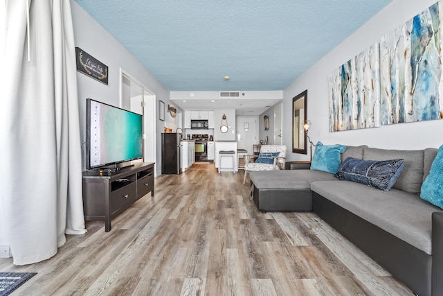 living area with visible vents, a textured ceiling, and light wood finished floors