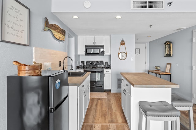 kitchen featuring a center island, visible vents, white cabinetry, a sink, and black appliances