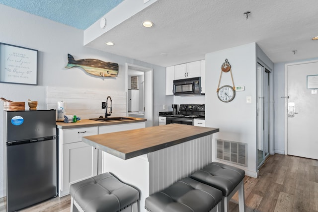 kitchen featuring visible vents, white cabinets, a breakfast bar area, black appliances, and a sink