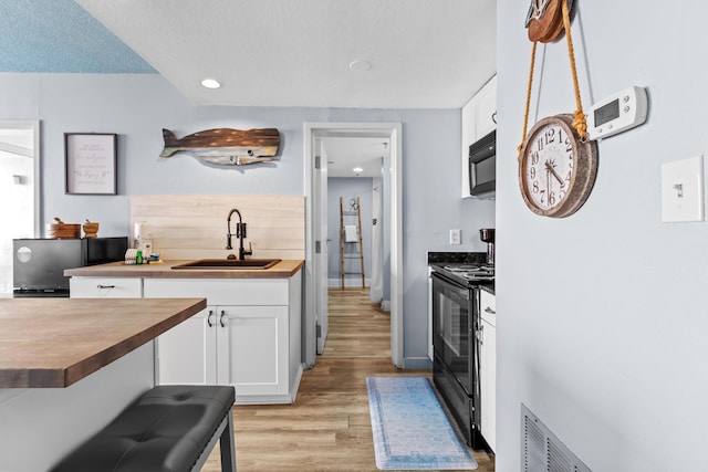 kitchen with black appliances, wood counters, white cabinetry, and a sink