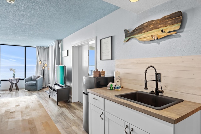 kitchen featuring a textured ceiling, a sink, wood counters, white cabinets, and light wood-type flooring