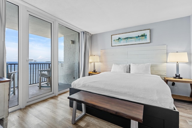 bedroom featuring light wood-type flooring, a wall of windows, a water view, and access to exterior