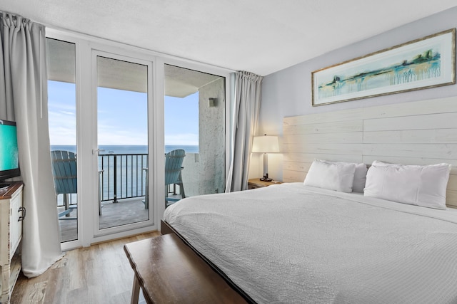 bedroom featuring a water view, light wood-type flooring, access to outside, and a wall of windows