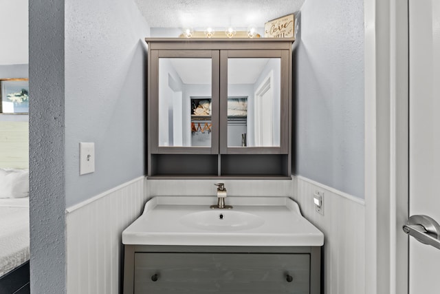 bathroom with a wainscoted wall, a textured wall, and vanity