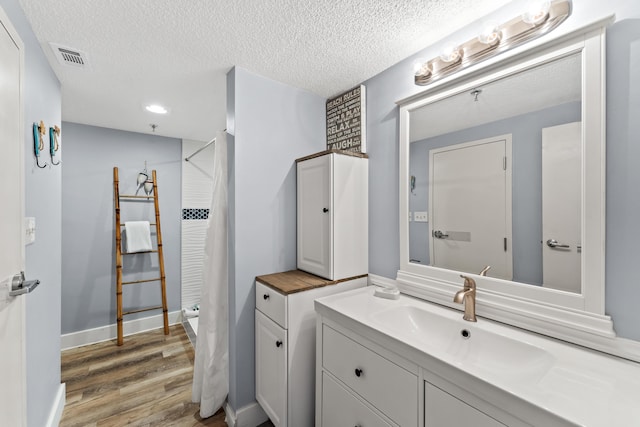 full bath featuring a textured ceiling, wood finished floors, visible vents, vanity, and baseboards